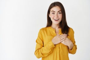 delighted-happy-young-woman-looking-with-admiration-joy-holding-hands-heart-appreciation-gift-standing-touched-white-wall